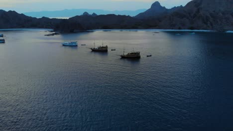 Barcos-Turísticos-En-La-Costa-De-La-Isla-Padar,-En-El-Parque-Nacional-De-Komodo-En-Indonesia,-Capturados-Desde-Un-Dron-Durante-La-Noche.