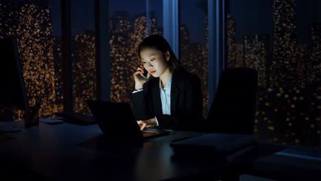 Young businesswoman working late at night in an office, on a phone call