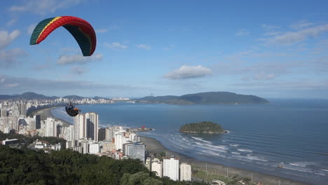 paraglider with colourful wing canopy flies low past launch site