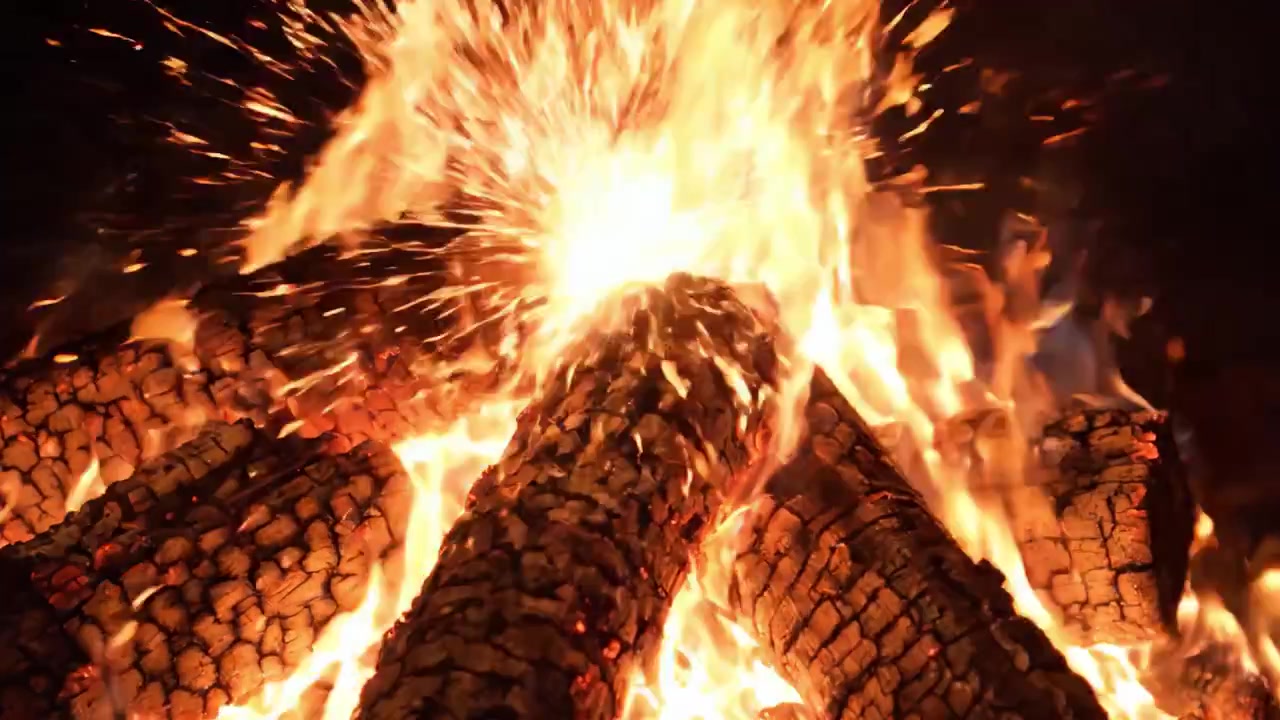 Fiamme affascinanti: un primo piano intenso di un falò scoppiettante con ceppi carbonizzati e scintille danzanti, che crea un'atmosfera calda e invitante nell'oscurità