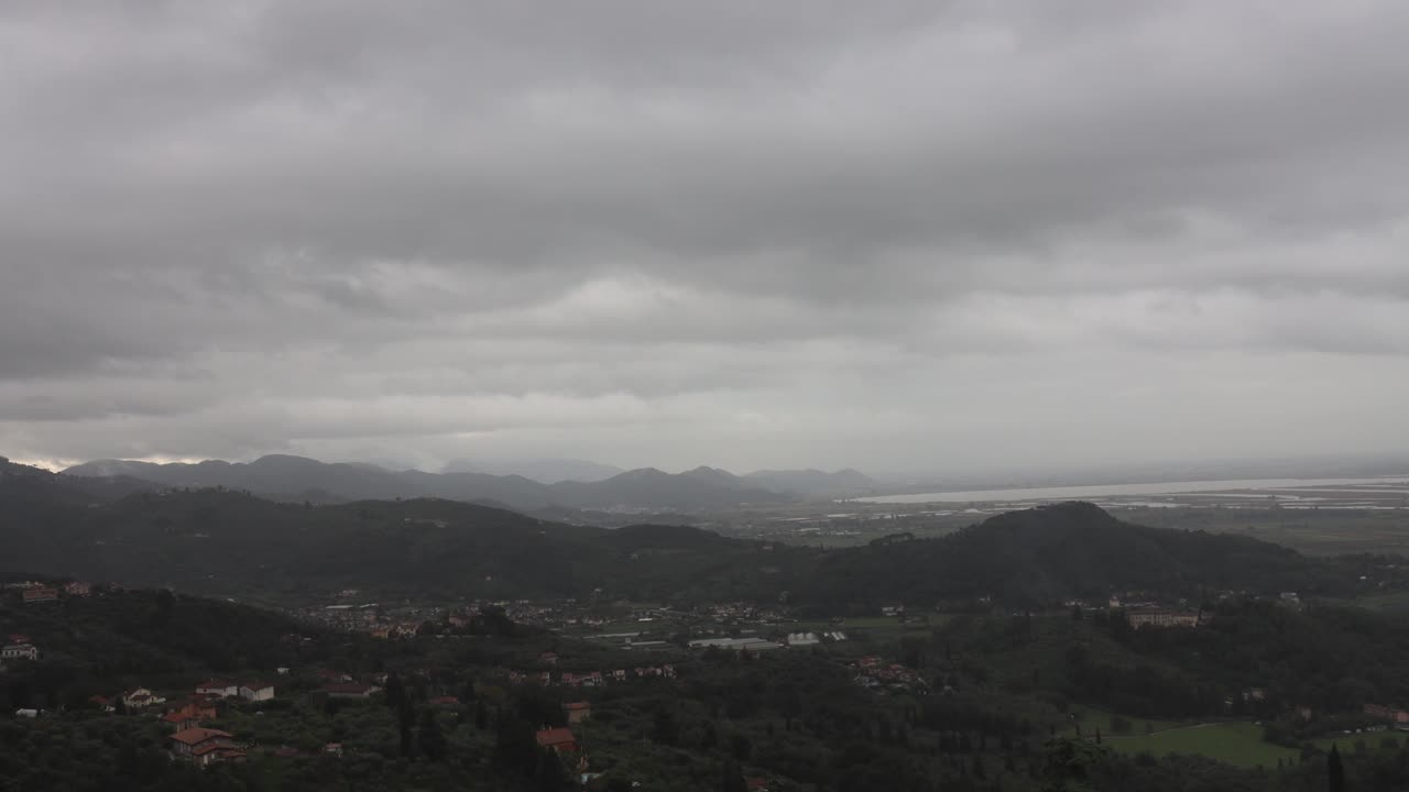 Time lapse of overcast clouds and rain over rural hilly landscape and villages near Via Reggio, Italy
