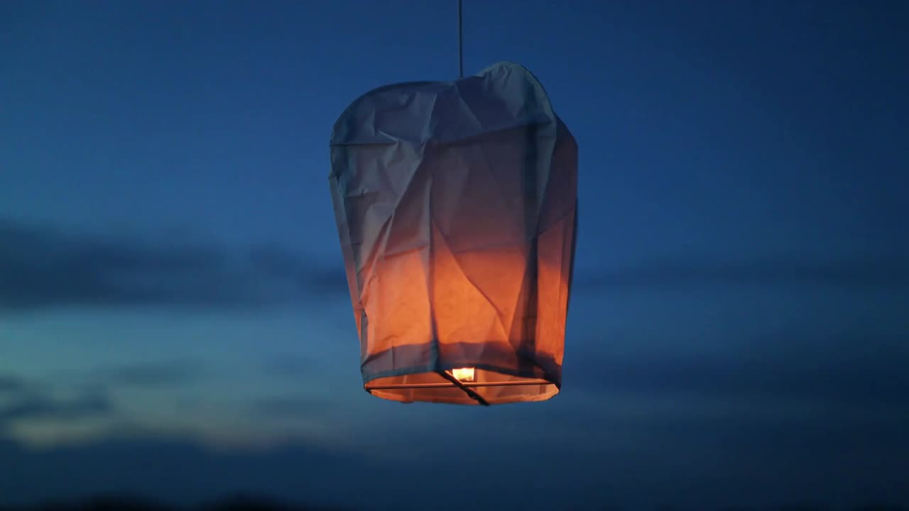 Api yang menyala, lampion terbang kertas bersinar dan bergoyang saat senja di atas cakrawala gelap, tali pengikat terlihat