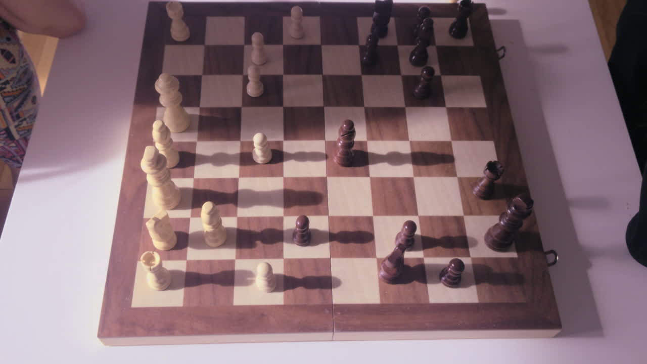 A top down POV view of a child's hand moving a wooden chess piece during a game with their mother. Authentic family bonding and educational play time at home in a cozy domestic setting