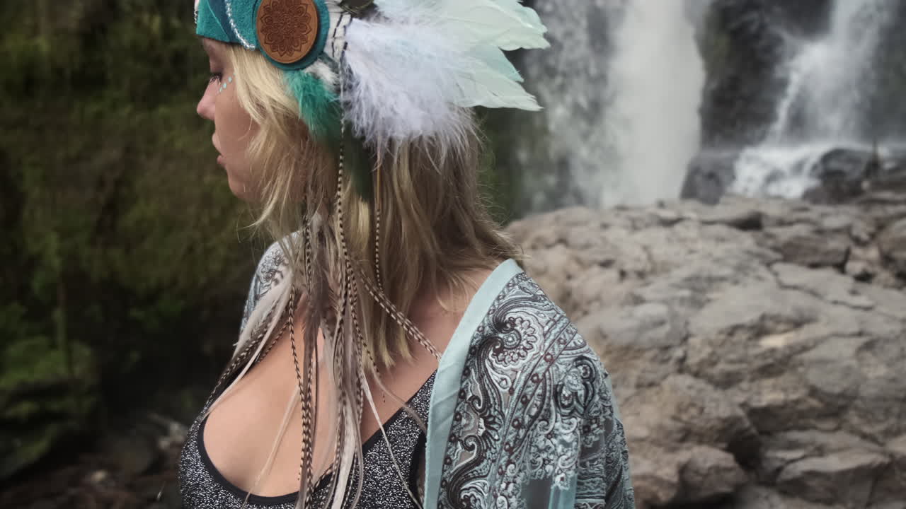 Woman with feather headband by a waterfall