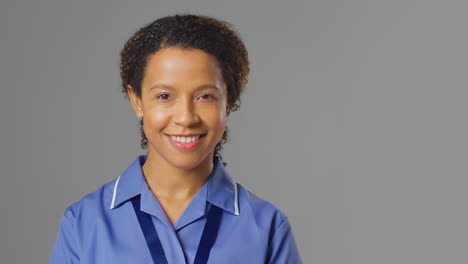 studio portrait of female nurse wearing uniform smiling at camera against grey background