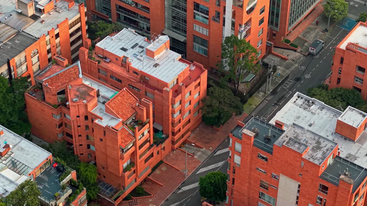 Low drone shot near orange rooftops in Bogotá, showing building tops, green trees, and city streets.