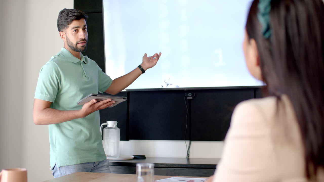 Presenting data, man holding tablet and explaining to colleague in office meeting