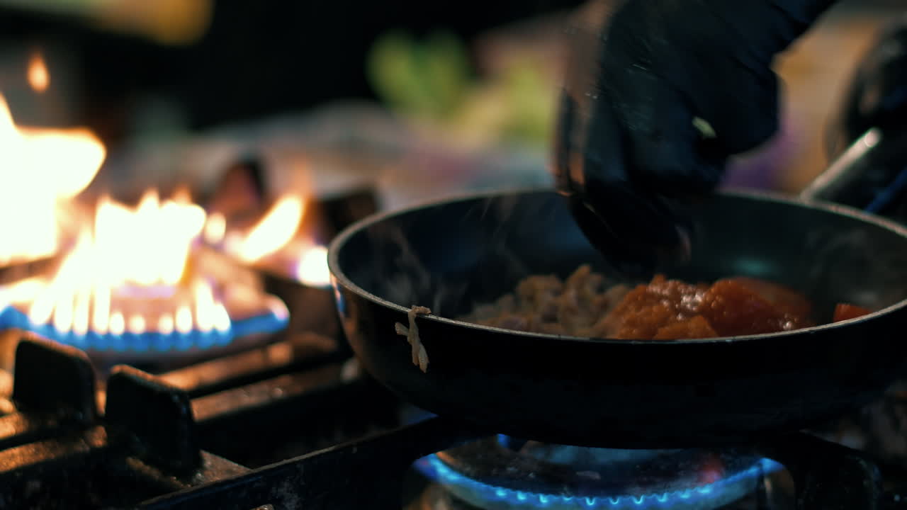 el chef de primer plano añadiendo ingredientes para la salsa. el cocinero masculino mezclando verduras en la sartén.