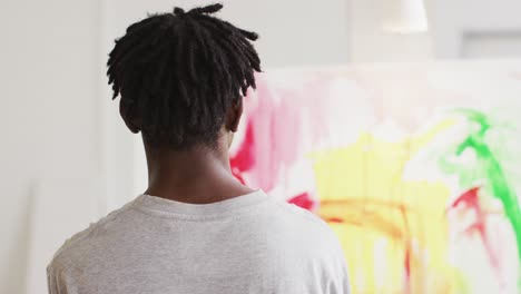 Rear-view-of-african-american-male-artist-painting-on-canvas-at-art-studio