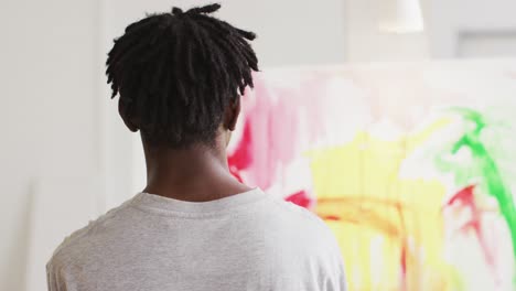 vista trasera de un artista masculino afroamericano pintando en lienzo en un estudio de arte