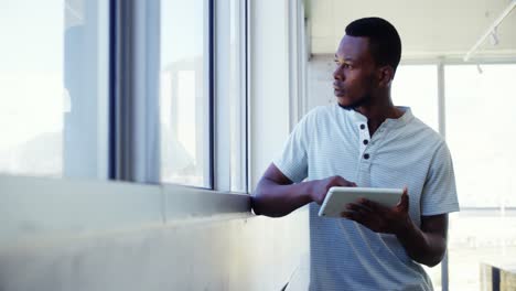 Executive-standing-near-window-and-using-digital-tablet