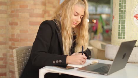 freelancer woman writing notes while working with laptop in cafe