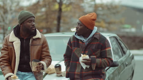 african american friends eating and speaking by car