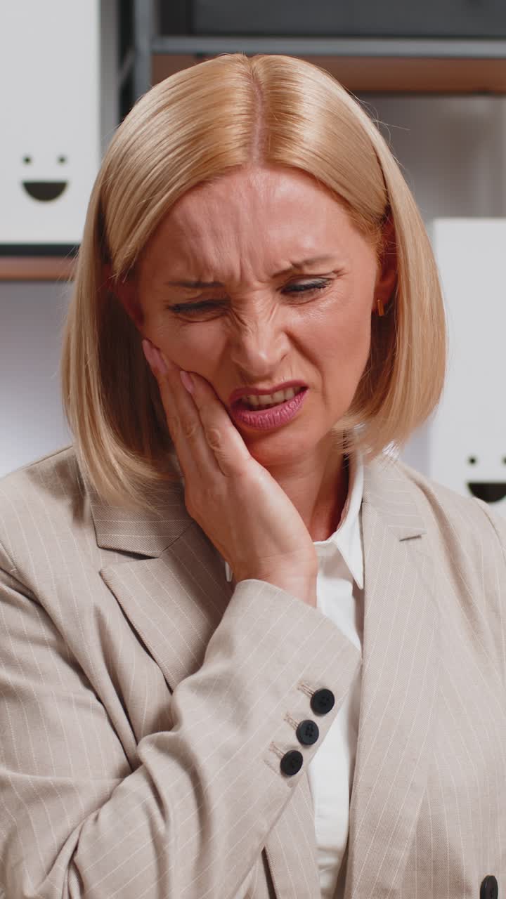 расстроенная зрелая бизнесменка в костюме страдает от зубной боли во время использования ноутбука на домашнем офисном столе