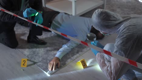 a forensic criminologist in a protective suit collects evidence and the detective examines the body.