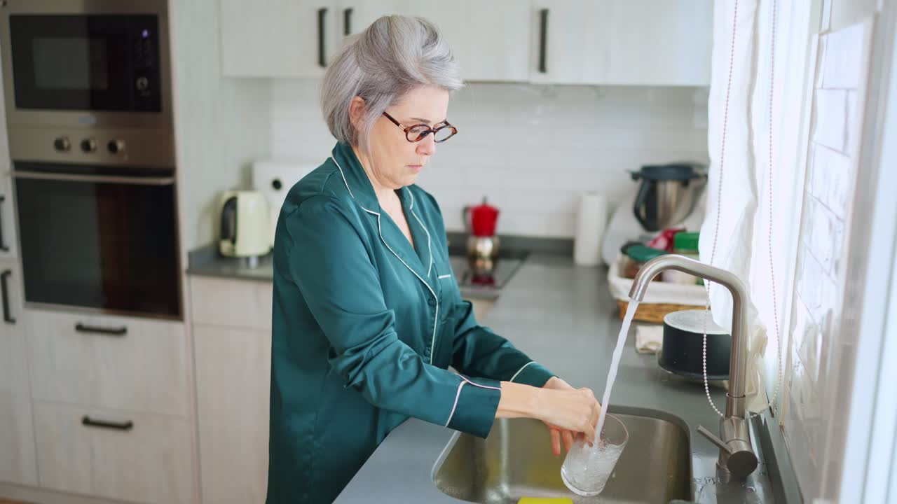 Donna anziana che lava un bicchiere nel lavandino di una cucina moderna