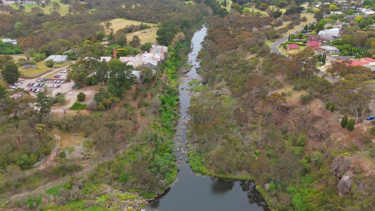 Drone footage showing Buckley Falls and narrow Barwon River passing through rocky green terrain near houses and parkland in Highton suburb of Geelong under soft daylight and cloudy sky