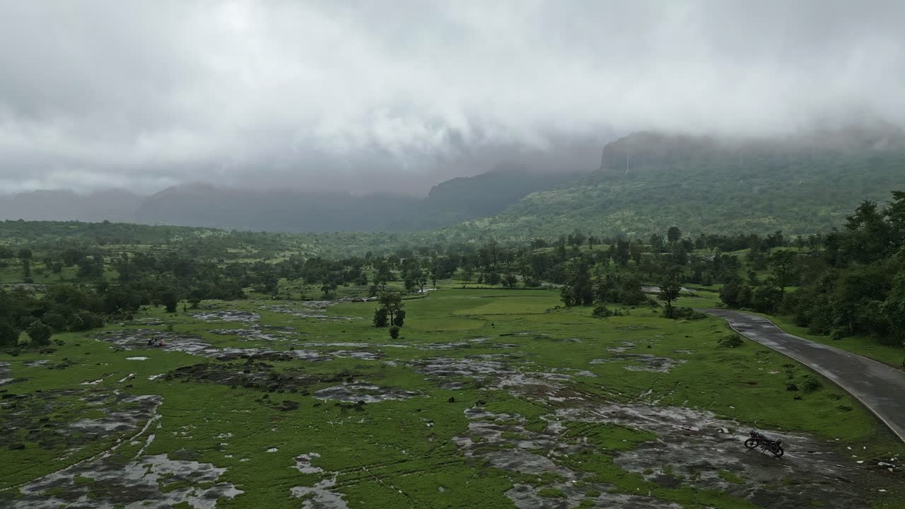 A breathtaking drone view of Bhandardara, Maharashtra, India, showcases lush green fields, misty mountains, and monsoon fog drifting through the landscape 4K