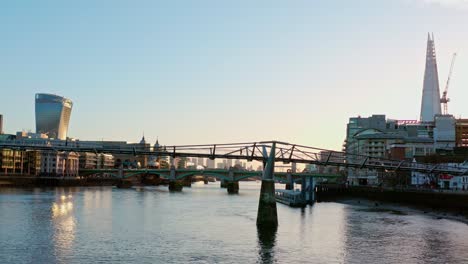 Toma-Aérea-De-Un-Hombre-Corriendo-En-Un-Puente-Peatonal-Del-Milenio-Sobre-El-Río-Támesis-Hacia-La-Ciudad-De-Londres-Al-Amanecer-Bajo