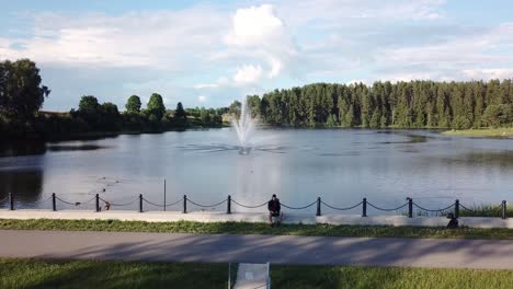 young man sitting and controlling drone with fountain in lake teperis in background during summer in smiltene, latvia