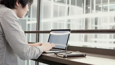 young asian business man using laptop computer and smartphone on wooden desk in working space. male hand typing on laptop keyboard. freelance lifestyle in digital age concept.