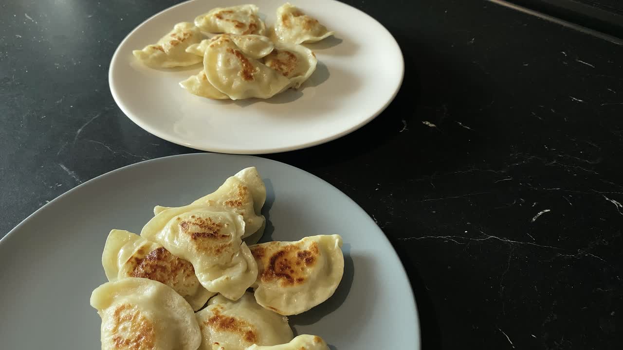 Close-up, put two plates with dumplings on black work top, slow motion,