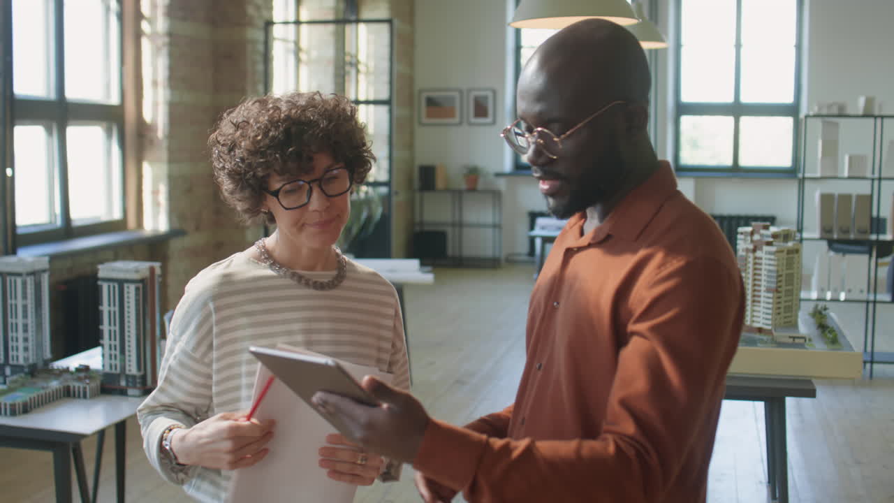 Architects collaborating and discussing project plans using a tablet in a modern office with building models
