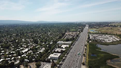 aerial view of suburbs dense trees rooftop houses pine trees cars freeway 101 marsh on left pivot right