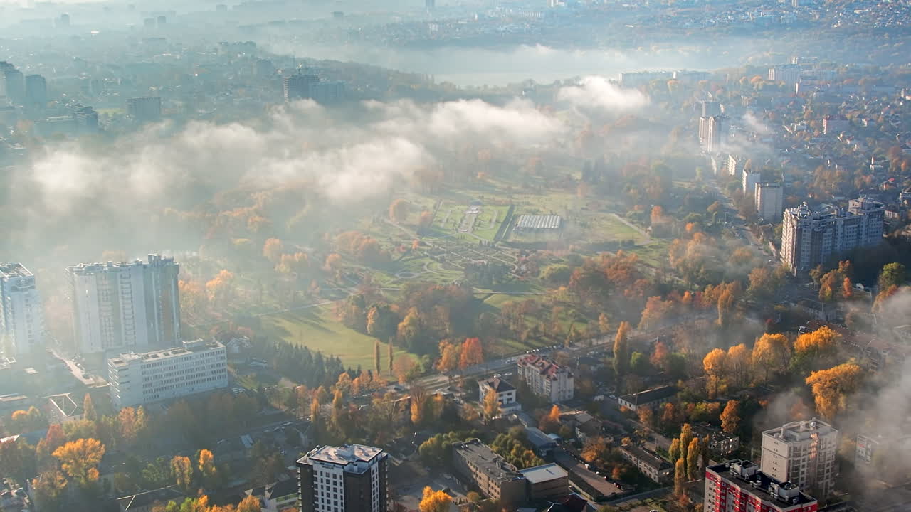 Aerial drone view of Chisinau at sunrise, Moldova. View of the city with fog in the air, multiple buildings around the Dendrarium park with yellowed trees