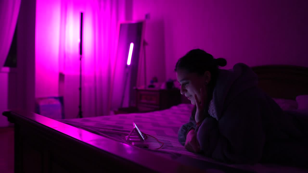 Donna al telefono in una camera da letto illuminata di viola