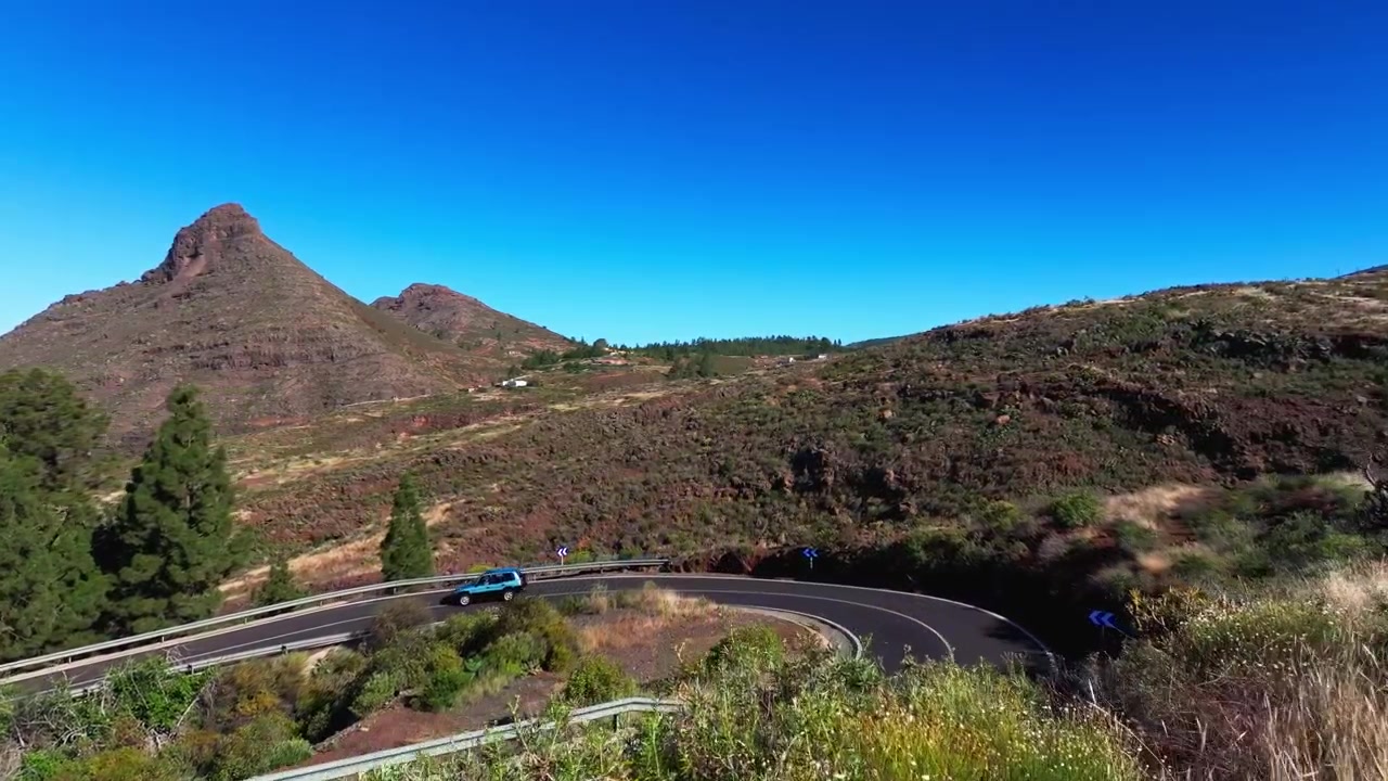 Veduta aerea che si eleva su colline vulcaniche, strada tortuosa e vegetazione rada sotto un cielo limpido.