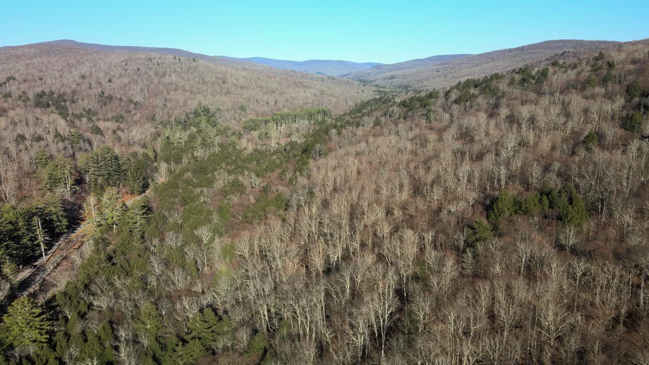 campo remoto con montañas, colinas, árboles desnudos, una carretera y una propiedad a fines del otoño