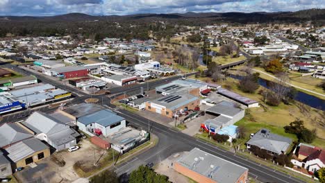 drone footage glides above a quiet australian town, revealing residential houses, parked cars, and commercial buildings under bright daylight with scattered clouds