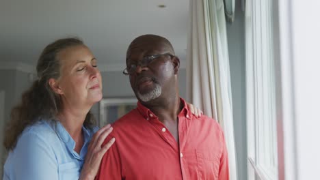 happy senior diverse couple wearing shirts and embracing in living room