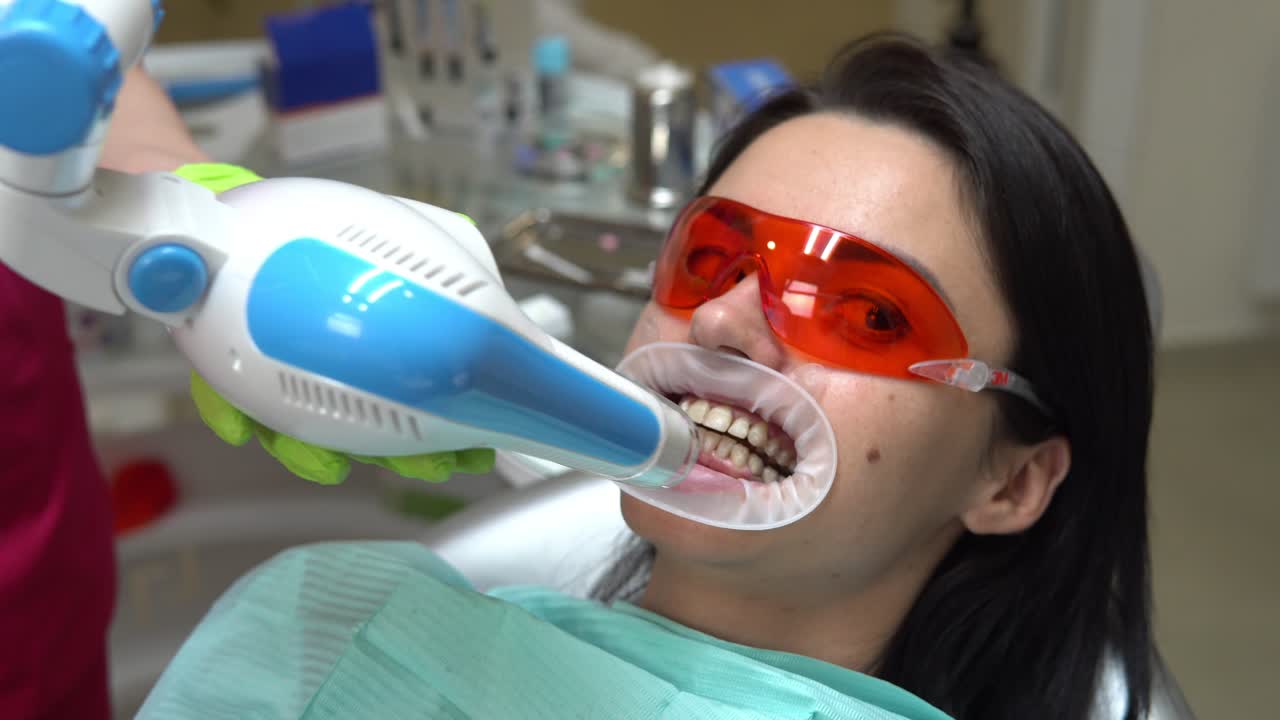 Young woman getting UV whitening at the dentist's office by an ultra violet machine. Shot in 4k