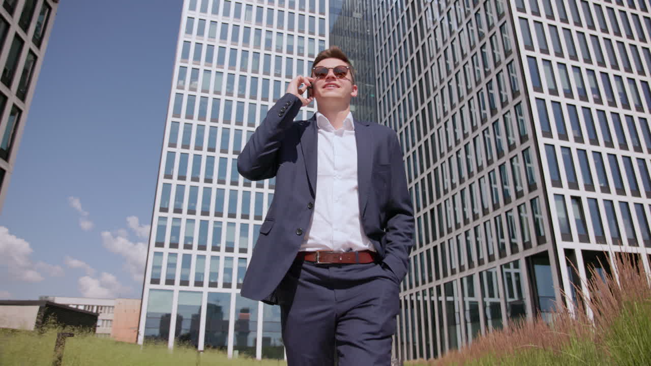 joven feliz en traje camina y habla por teléfono, vista frontal del suelo