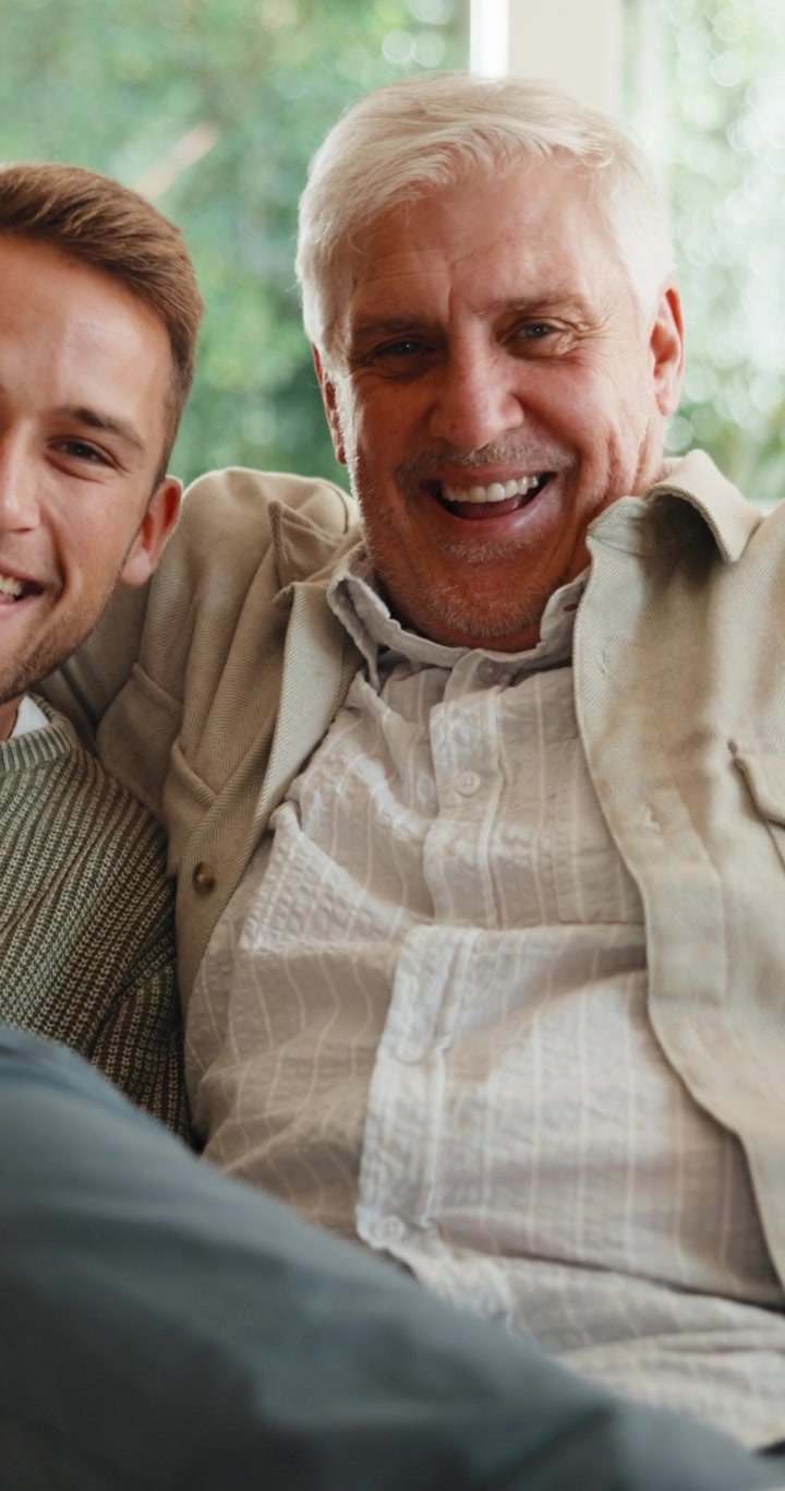 Happy Father and Adult Son Laughing Together on Sofa