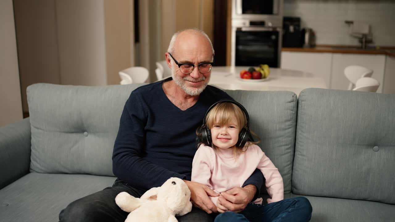 retrato de una niña pequeña con auriculares con su abuelo mientras está sentada en el sofá