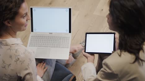 Diverse-female-colleagues-using-laptop-and-tablet-with-copy-space-on-screens-in-office,-slow-motion