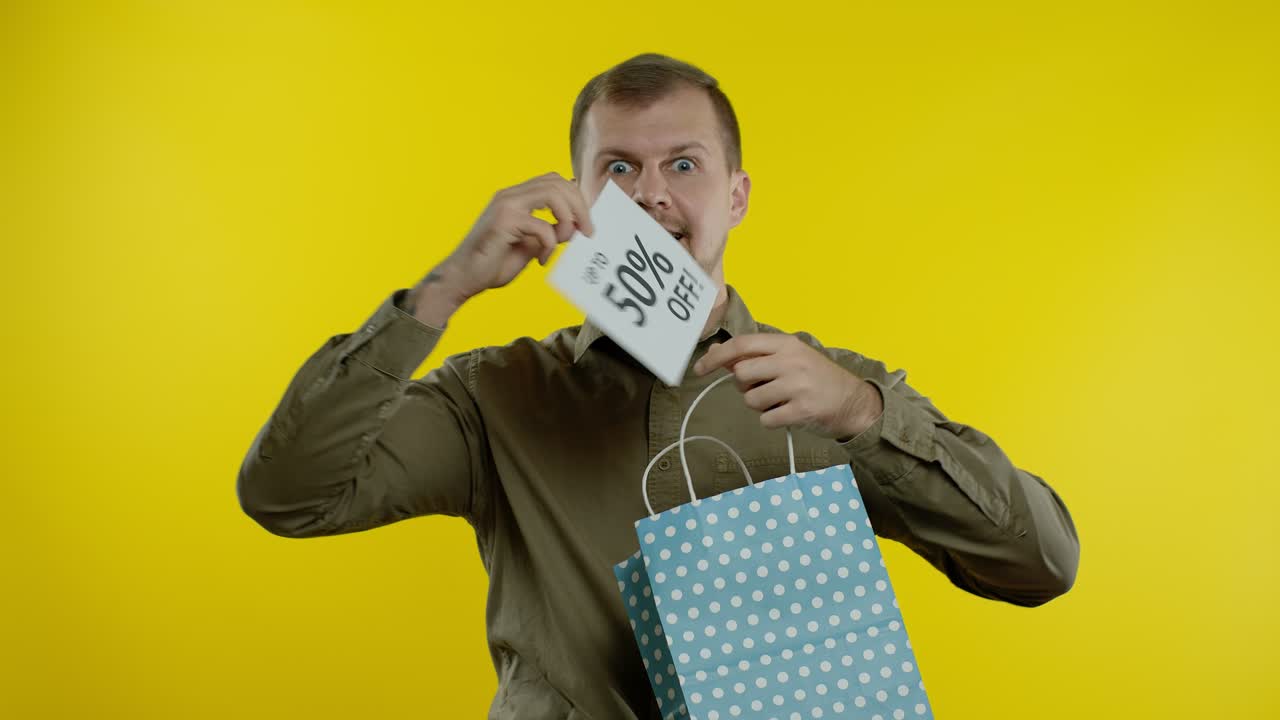 hombre feliz mostrando hasta un 50 por ciento de descuento inscripción de la bolsa de compras, sonriendo, regocijándose descuentos