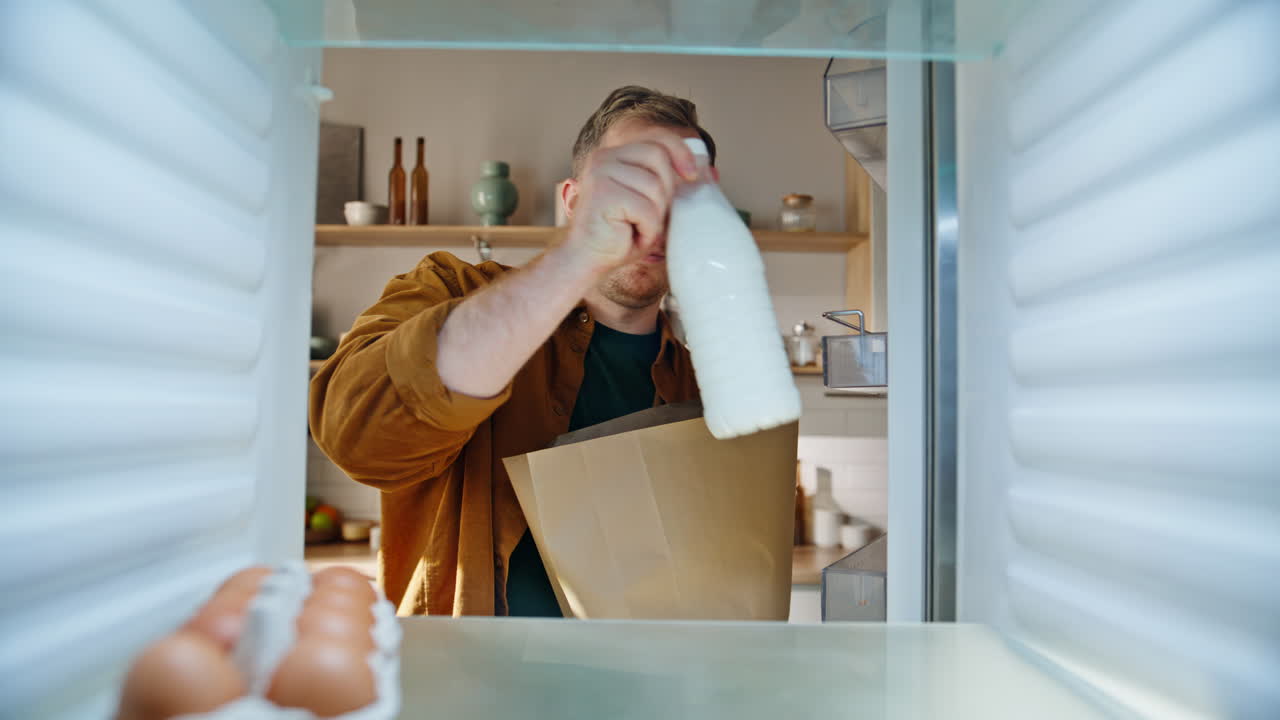 Mann füllt leeren Kühlschrank aus der POV-Perspektive, Nahaufnahme. Lächelnder Mann packt Lebensmittel aus