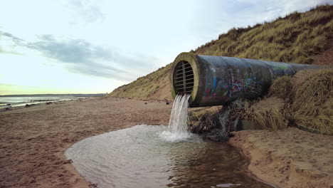 culvert discharging water into a stream on a beach side view