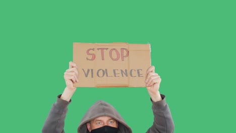 protestant man showing stop violence sign on social rally on green screen background. man in black mask and hood with holding cardboard on political uprising, chroma key background