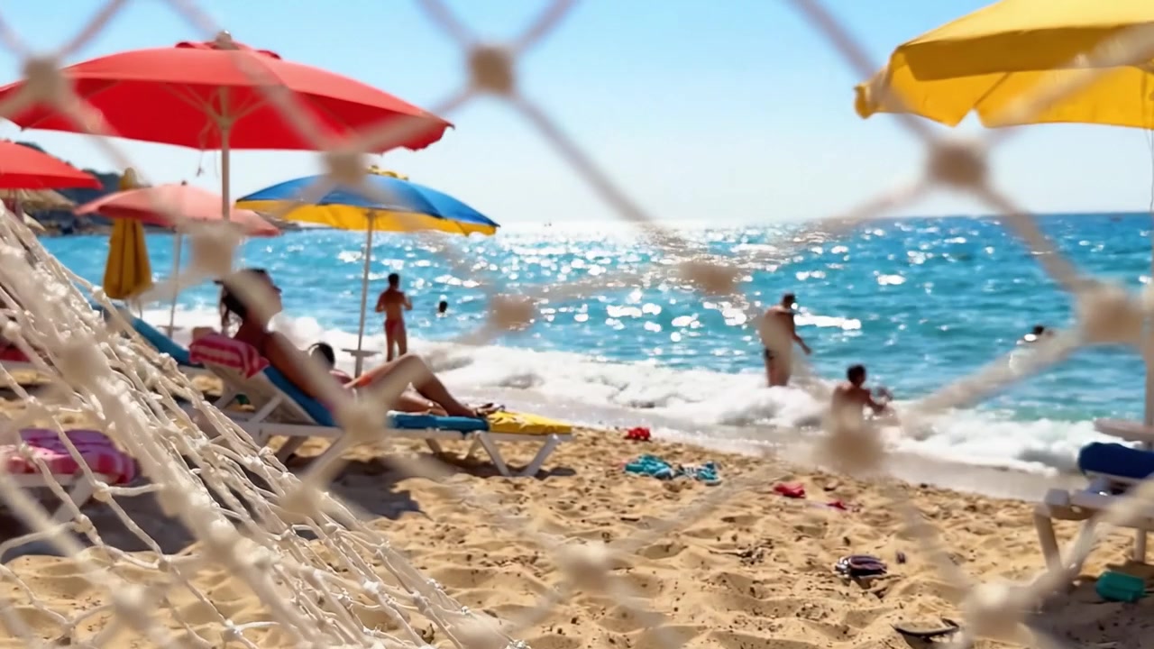 Levendige Strandscène: Ontspannen onder Kleurrijke Parasols met Zachte Golven en Zonaanbidders Genietend van de Warmte van een Stralende Zomerdag