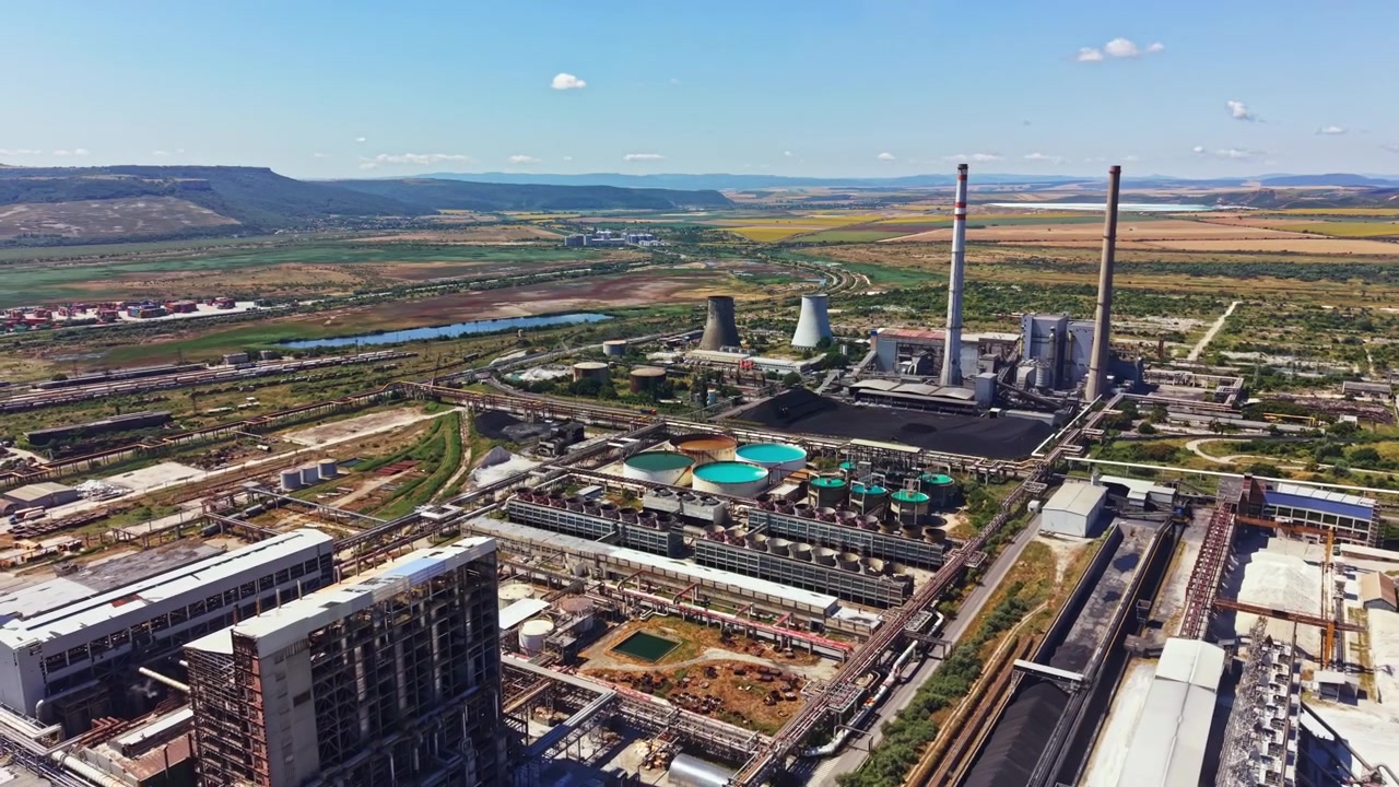 Zona industrial con central eléctrica y tanques de almacenamiento cerca de un río durante el día con campos verdes al fondo