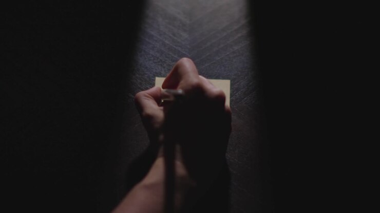 Slow motion close up footage of a hand writing out "February" on a paper note and placing it on a table. Shot in dramatic lighting for an impressive title or transition