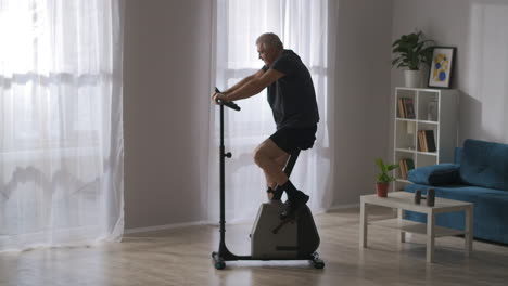 old man is training on exercise bike in living room rehabilitation after injury keeping health of body breathing and cardio workout