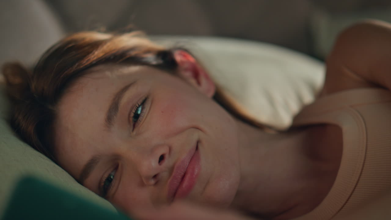 Girl looking cellphone waking up in bed close up. Happy woman reading smartphone