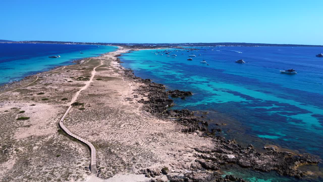 Punta des Borronar beach on Formentera Ibiza island with yachts mooring in clear turquoise water. Smooth aerial view flight overflight flyover pull in drone