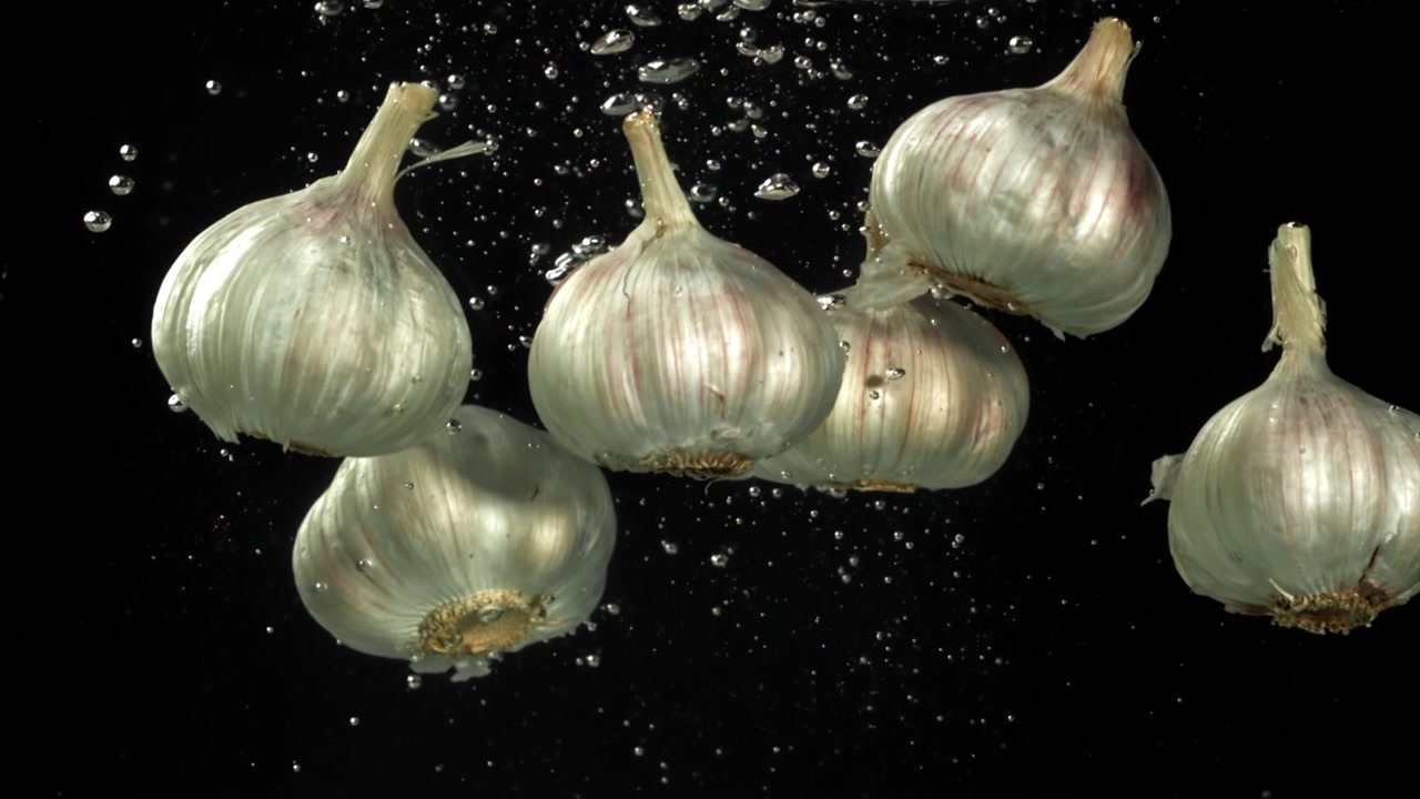 Bulbi d'aglio freschi sommersi nell'acqua con bolle su sfondo nero.